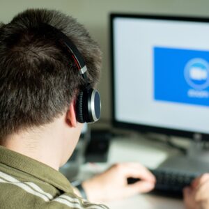 Man with headphones looking on the monitor with zoom cloud meetings logo.